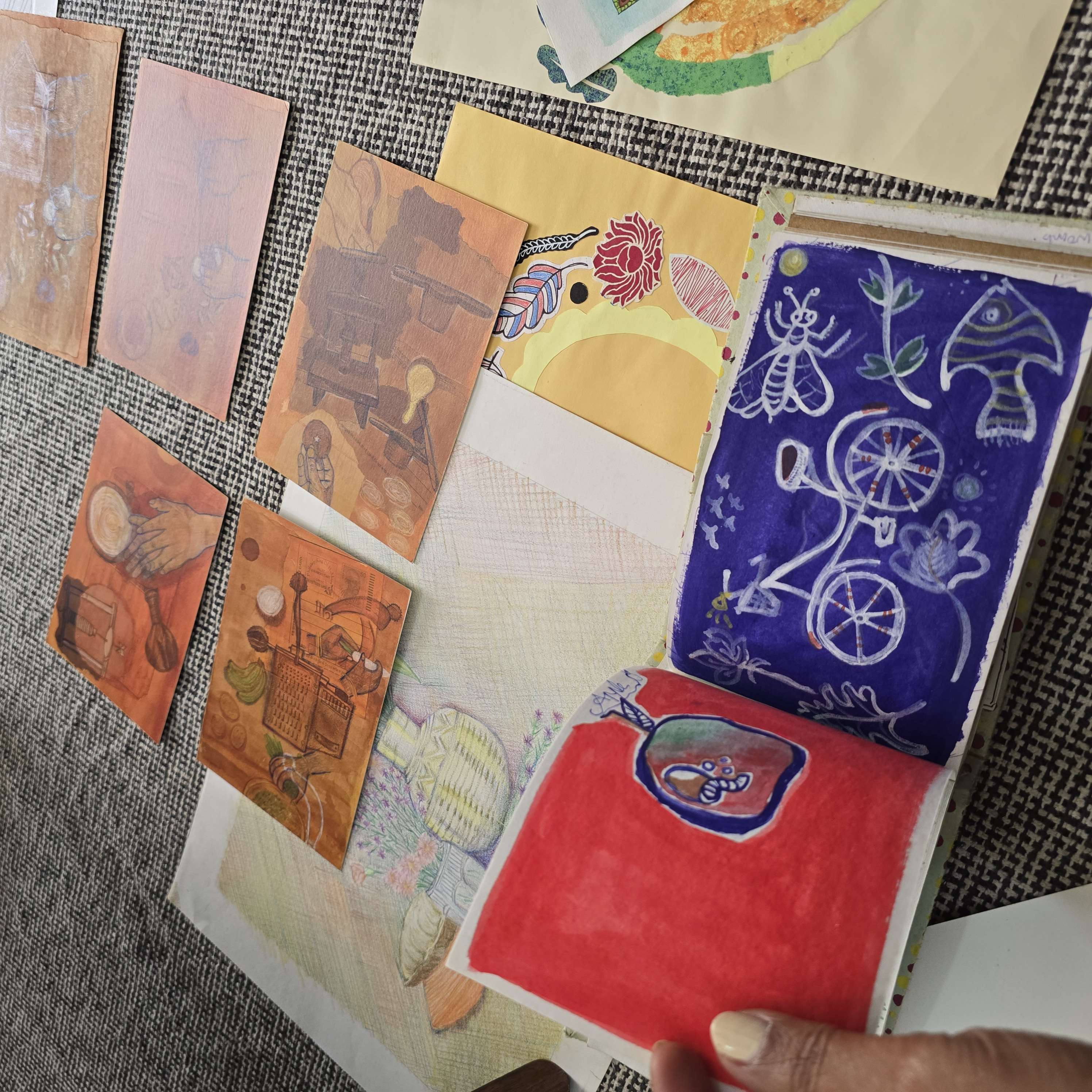 Open sketchbook with illustrated pages placed among art prints and papers